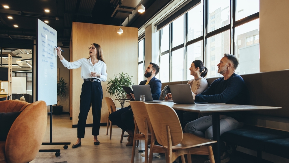 Break-out meeting. A woman stands at a white board writing down notes as the group explores different aspects of risk assessment. 
