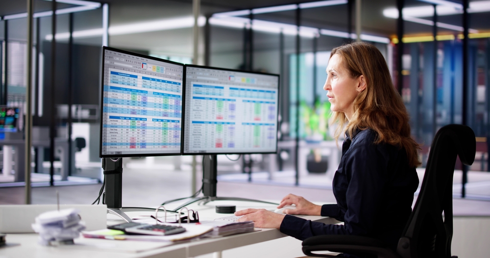 woman sitting at a desk with two monitors preparing a financial audit